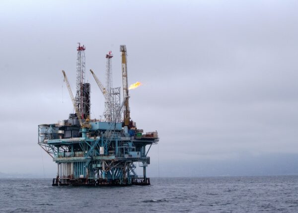 An oil rig at sea showing gas or oil being burnt off from an outlet on the facility and a number of tall metal structures. 