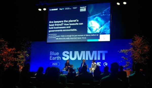 Ana Carolina Salomão Queiroz of Pogust Goodhead and Laura Clarke of Client Earth on stage at the Blue Earth Summit backed by a blue-lit event stage and big screen.